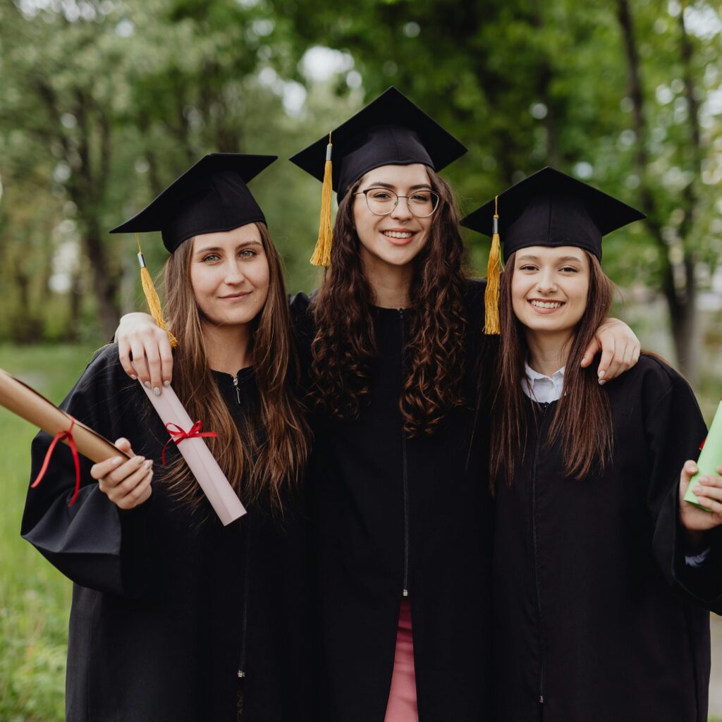 Three female graduates in caps and gowns celebrating their academic success outdoors.